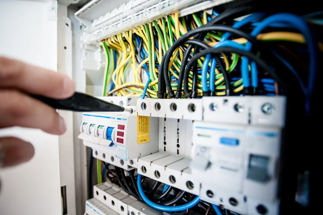 Main approchant un tournevis des appareils modulaires d’un tableau électrique, au milieu de fils colorés