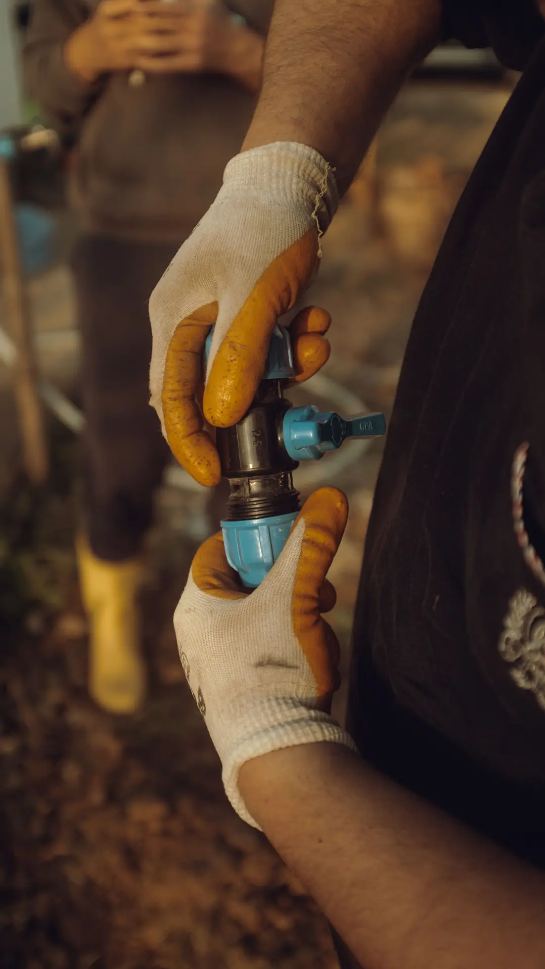 Mains gantées assemblant un raccord bleu à vanne sur une conduite d’eau, sur un chantier en extérieur